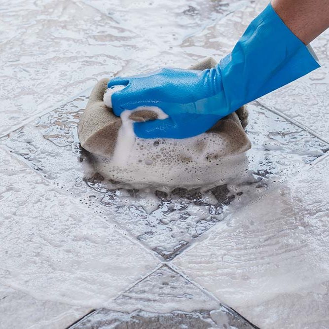 Hand of man wearing blue rubber gloves is using a sponge cleaning the tile floor